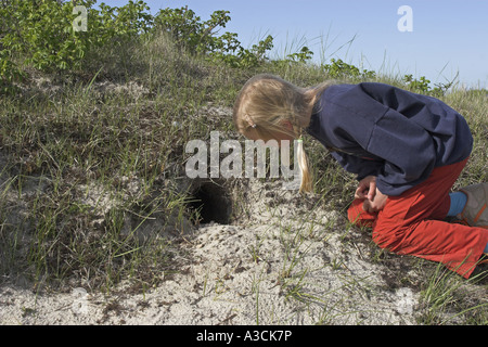 Lapin de garenne (Oryctolagus cuniculus), fille de genou devant un terrier de lapin Banque D'Images