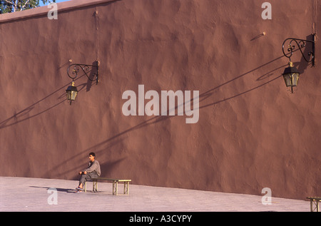 Une figure solitaire est assis sur un banc près de la mosquée de Koutoubia Maroc Marrakech très longues ombres sur le mur Banque D'Images