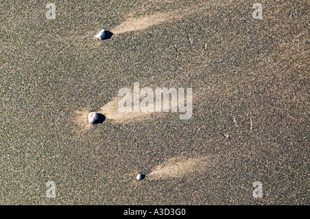 Trois cailloux sur la rive causant des formations dans le sable de l'écoulement de l'eau Banque D'Images