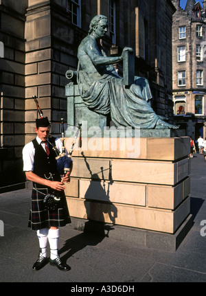 Homme jouant de la cornemuse à côté de statue de David Hume (par le sculpteur Alexander Stoddart) à l'extérieur de Haute Cour de justicier à Edimbourg Ecosse UK Banque D'Images