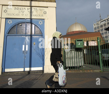 Femme musulmane en passant en face de l'entrée de la Synagogue de la rue Fieldgate et East London mosque dans l'arrière-plan Banque D'Images