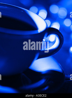 Close up de tasse à café et soucoupe avec les lumières de la ville en arrière-plan baigné de lumière d'un bleu profond. Banque D'Images