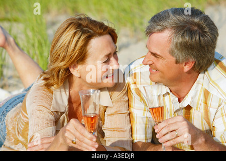 Close-up of a young couple lying on the beach et holding champagne flutes Banque D'Images