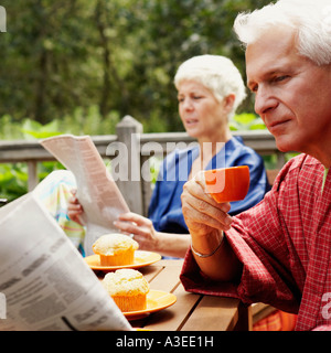 Close-up of a young man holding a cup et lire un journal avec une femme senior dans l'arrière-plan Banque D'Images