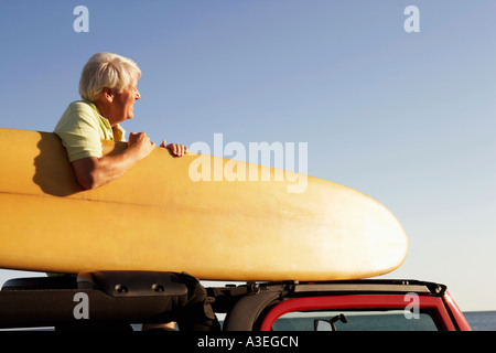 Portrait d'un homme mûr assis dans un véhicule utilitaire sport et la tenue d'un surf Banque D'Images