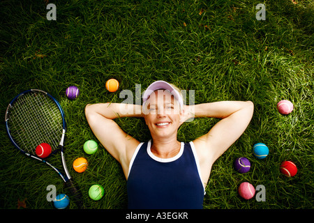 High angle view of a young woman lying on the grass avec des balles de tennis et une raquette de tennis Banque D'Images
