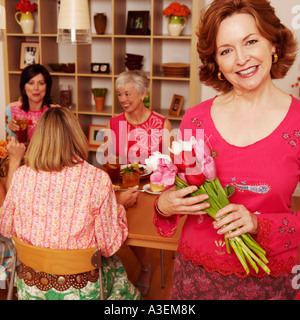 Portrait of a young woman holding a bouquet de fleurs et ses amis assis à la table à manger dans l'arrière-plan Banque D'Images