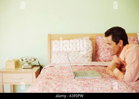 Portrait d'un homme mûr couché sur le lit en face d'un laptop and smiling Banque D'Images