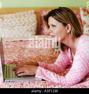 Portrait of a young woman lying on the bed et l'aide d'un ordinateur portable Banque D'Images