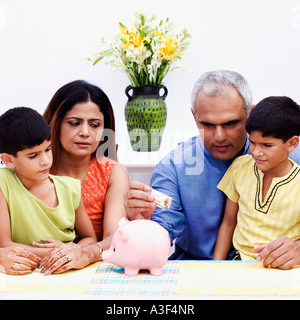 Mid adult man mettant un monnaie indienne remarque dans une tirelire avec sa femme et ses deux fils à côté de lui Banque D'Images