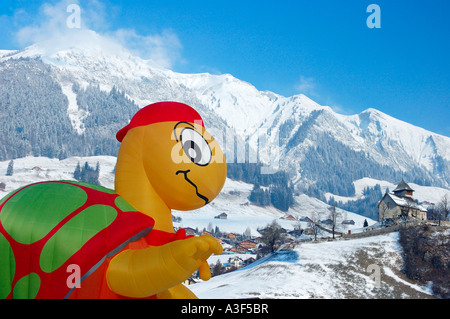 Un ballon gonflé d'être comique au château d'Oex de montgolfières, qui pèse sur le village, les Alpes enneigées en arrière-plan Banque D'Images