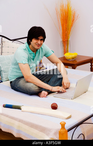 Portrait d'un jeune homme à l'aide d'un ordinateur portable sur le lit Banque D'Images