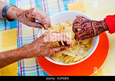 Close-up de trois mains tatouées au henné en tenant un bol de croustilles de pommes de terre Banque D'Images