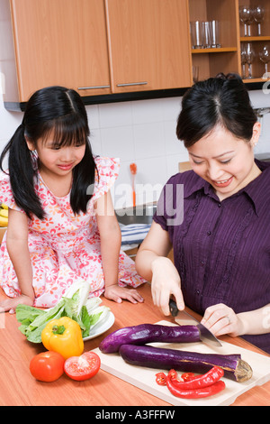 Jeune femme couper des légumes avec sa fille assis sur le comptoir de la cuisine Banque D'Images