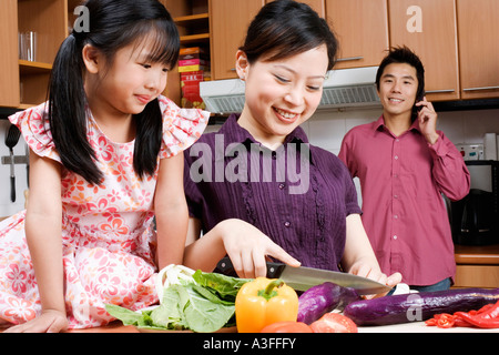 Close-up of a young woman cutting vegetables avec sa fille, assis près d'elle Banque D'Images