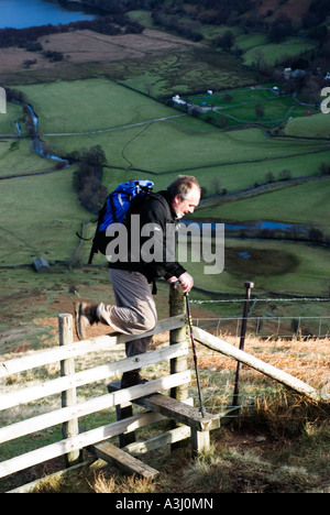 Walker mature traverse un stile dans le Lake District Banque D'Images