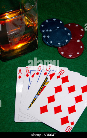 Cartes de poker montrant un flush royal avec des jetons de casino et un verre de whisky sur les rochers tout de feutrine verte table à cartes Banque D'Images