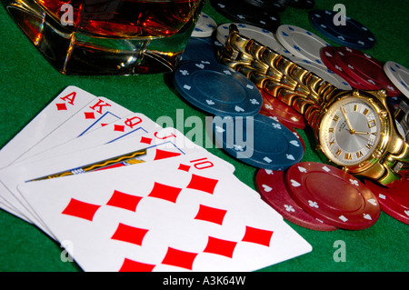 Cartes de poker montrant un flush royal avec jetons de casino une montre et jeté dans un verre de whisky sur les rochers tous sur une feutrine verte ca Banque D'Images