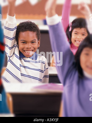 African American latino asiatique students raising hands in elementary school classroom Banque D'Images