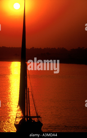 Felouque glisse le long fleuve du Nil en Egypte lumière coucher du soleil orange Banque D'Images