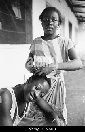 Une fille d'un tressage de cheveux des garçons dans un composé dans la Gambie Bakau Kachikally Afrique de l'Ouest Banque D'Images