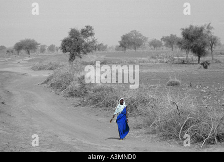 Femme autochtone voilée marcher seule le long d'une route poussiéreuse au Burkina Faso anciennement Haute-volta Banque D'Images