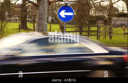 Le bleu de l'tournez à gauche panneau routier avec un excès de voiture cours des arbres en arrière-plan Banque D'Images