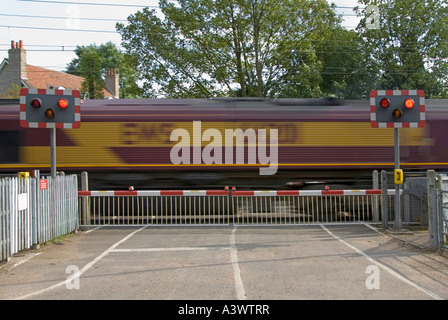 Les voies de chemin de fer rouge clignotant signe d'avertissement de passage à niveau portes barrière country road train de marchandises de l'EWS de flou Margaretting Essex England UK Banque D'Images