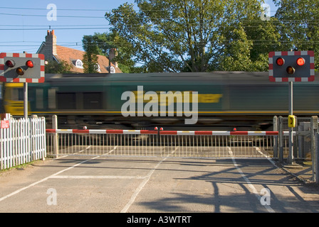 Les voies de chemin de fer rouge clignotant signe d'avertissement de passage à niveau portes barrière country road train Freightliner flou Margaretting Essex England UK Banque D'Images