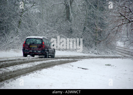 La ligne de chemin de campagne hiver arbres flocons de neige tombent sur votre location de voiture sur la neige mouillée et de neige couverts route avec feux arrière sur campagne de l'Essex au Royaume-Uni météo Banque D'Images