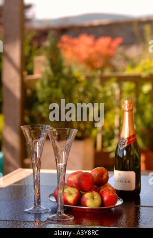 Une BOUTEILLE DE CHAMPAGNE BOLLINGER AVEC DEUX FLÛTES ET UN BOL DE POMMES SUR UNE TABLE DANS UN PATIO UK Banque D'Images