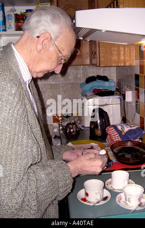 Senior Male de prendre une tasse de thé par ajout de sucre dans la tasse avant que le lait. Banque D'Images