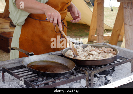 Deux casseroles sur un feu de charbon avec une main de femme tenant une spatule pour retourner la viande Banque D'Images