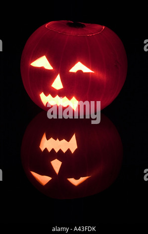 Un effrayant halloween citrouille éclairée par la bougie de l'intérieur sur un fond noir avec reflet Banque D'Images