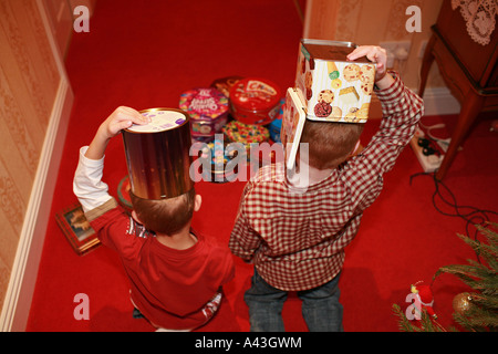 Deux jeunes enfants garçons en métal recyclable en acier vide bonbon sucré tins sur leurs têtes comme soldats de plomb à la maison Banque D'Images