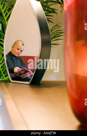 Femme LISANT À LA MAISON REFLÈTE DANS UNE LAMPE EN MIROIR Banque D'Images