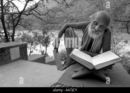 Un dévot hindou lit un livre sur la rive de la rivière Sainte Gange à Rishikesh en Inde Banque D'Images