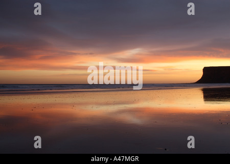 Vue de la plage à Saltburn dans Yorkshire du Nord avec le lever du soleil dans le ciel des couleurs reflétée sur le sable humide à la recherche de vers Falaise Banque D'Images