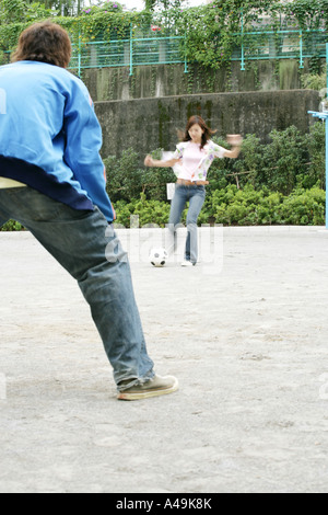 Jeune femme botter un football avec un jeune homme en face d'elle Banque D'Images