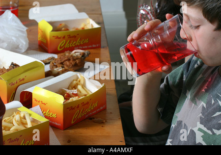 Un garçon de huit ans de boire une boisson avec ses plats à emporter repas de poulet et frites à la maison, février 2006 . Banque D'Images