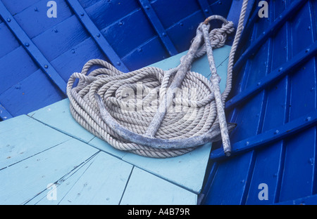 Détail de la petite ancre de métal couché sur sa corde enroulée soigneusement à l'avant d'un petit bateau en bois peint bleu clair et foncé Banque D'Images