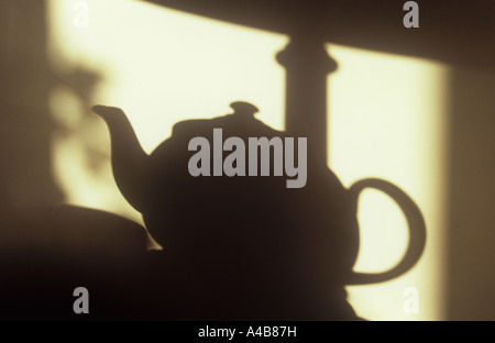 Ombre sur mur crème dans une lumière chaude de théière avec tasse et une lampe de table et avec le feuillage à window Banque D'Images