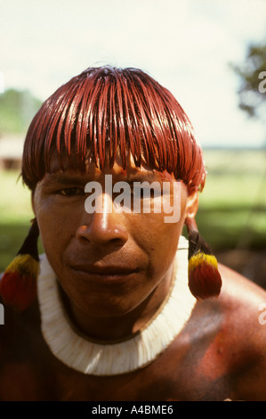 Posto Leonardo, Xingu, au Brésil. Homme avec cheveux teints à l'Urucum rouge et coller des plumes colorées d'oreille ; tribu Xingu. Banque D'Images