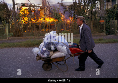 La Géorgie, d'Otchamtchira, 28 septembre 1993 : un homme pousse ses biens dans une brouette devant une maison en feu comme géorgiens d'Otchamtchira abandonner le jour après la chute de Soukhoumi à forces séparatistes abkhazes. Banque D'Images