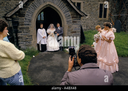 COUPLE MARIÉ DEBOUT DANS LA PORTE DE L'ÉGLISE AYANT UNE PHOTOGRAPHIE PRISE AVEC UNE FEMME MEMBRE DU CLERGÉ, Banque D'Images