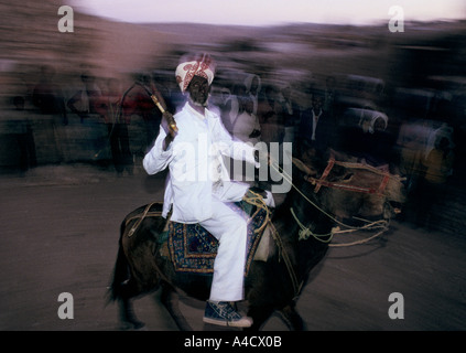 Invité à un mariage musulman Adi Caieh vagues l'Érythrée un fouet qu'il chevauche son âne dans une procession, Nov 1990 Banque D'Images