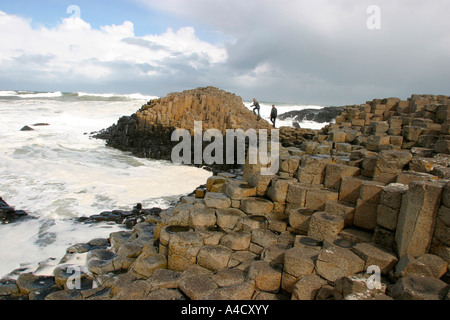 Le comté d'Antrim Giants Causeway couple climbing sur rochers entourés par de gros surf Banque D'Images
