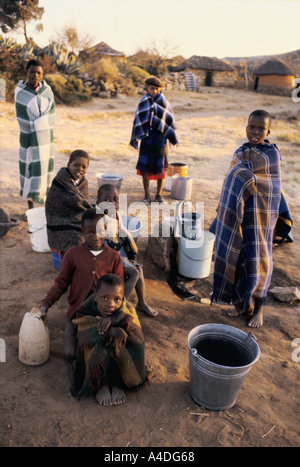 Les gens et les enfants enveloppés dans des couvertures, recueillir avec des seaux et récipients pour recueillir l'eau. Le Lesotho, l'Afrique du Sud Banque D'Images