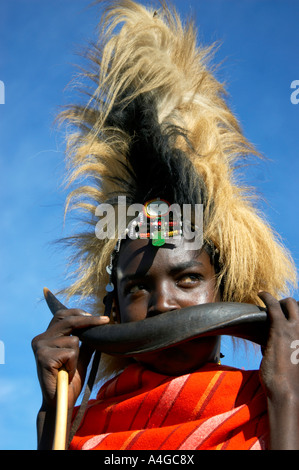 Un homme Masai souffle dans une corne d'antilope dans le village Masai Mara au Kenya. Banque D'Images