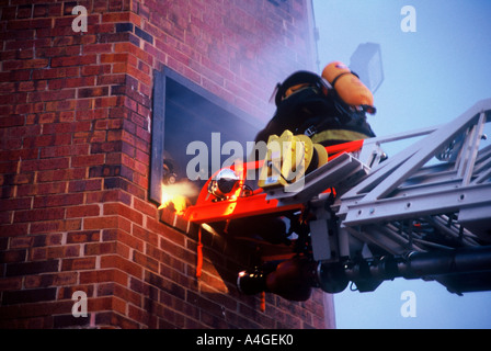 Fire camion échelle étendue à une fenêtre avec un pompier sur l'échelle, en entrant dans la fenêtre Banque D'Images